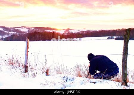 Fotograf im Schnee auf der Wiese lag und nimmt ein Bild der fantastischen Sonnenuntergang über dem gegenüberliegenden Hügel Stockfoto