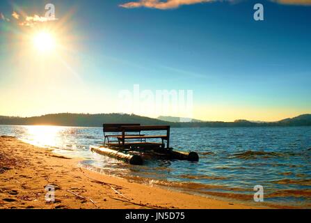 Verlassene alte Tretboot verfing sich auf sandigen Strand bei Sonnenuntergang. Insel mit Wald am Horizont. Stockfoto