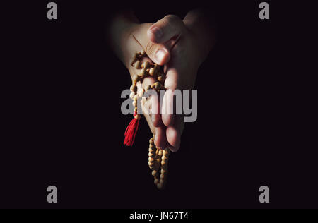 Hände gefaltet im Gebet auf schwarzem Hintergrund isoliert. Der Priester im Gebet. Rosenkranz in den Händen der Männer Stockfoto