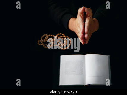 Männliche Hand gefaltet in Gebet Rosenkranz Perlen Closeup und Koran auf Hintergrund. Stockfoto
