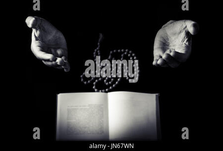 Männliche Hand gefaltet in Gebet Rosenkranz Perlen Closeup und Koran auf Hintergrund. Schwarz / weiß Retro-Foto Stockfoto