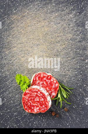 Scheiben von ausgehärteten Rohwurst mit Kräutern und Pfefferkörner auf schwarze Schneidebrett Stockfoto