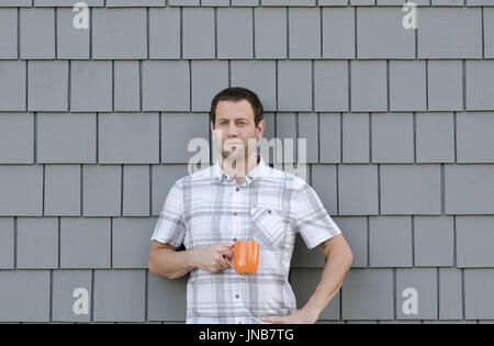 Mann mit Hand auf seiner Hüfte Holding eine Kaffeetasse gegen eine graue Wand. Stockfoto