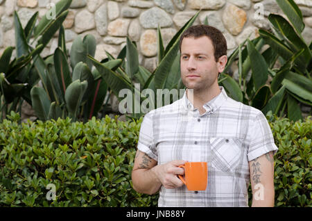 Hoffnungsvolle Mann draußen halten eine orange Kaffeebecher auf die Seite. Stockfoto