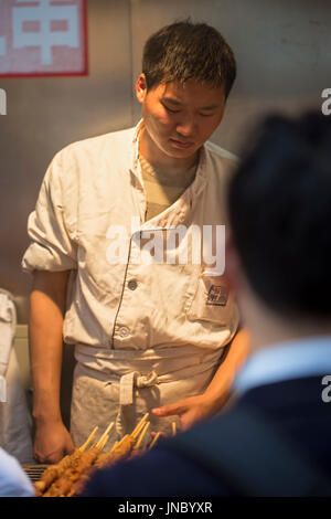 Chinesischen Verkäufer in weißer uniform auf Garküche, chinesischen traditionellen Lebensmittelmarkt. Wangfujing, Chaoyang District, Beijing, China, 5. April 2016 Stockfoto