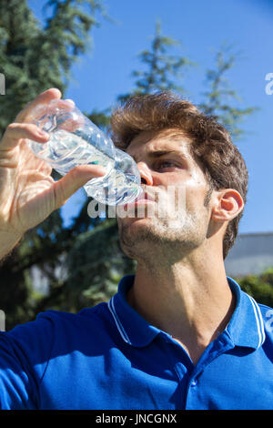 Profi-Tennisspielerin trägt einen blauen Polo ist Tennis Match Trinkwasser aus einer Flasche ruhen. Er sitzt vor den Tennisplätzen. Stockfoto