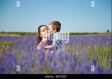 niedlichen kleinen Jungen küssen seine schöne Mutter mit ihren Augen geschlossen mit Freude auf das Lavendelfeld Stockfoto