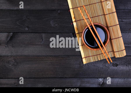 Hintergrund für Sushi. Bambusmatte und Sojasauce auf schwarzer Holztisch. Draufsicht mit Textfreiraum Stockfoto