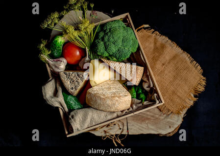 Kraft hausgemachter Käse mit Gemüse in einer Holzkiste auf dem dunklen Hintergrund Stockfoto