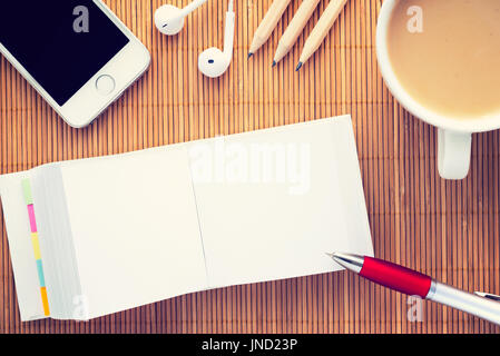 Arbeitsplatz mit geöffneten leeren Notebook für Notizen. Kaffee, Smartphone, Kopfhörer und Notizblock auf Bambus Holz Hintergrund; Draufsicht mit Textfreiraum. Vint Stockfoto