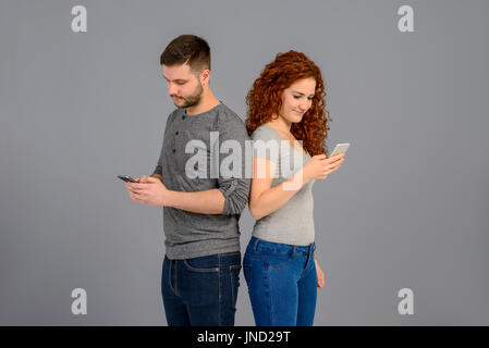 Ein schönes junges Paar Rücken an Rücken stehend, während halten und mit ihren smartphones Stockfoto