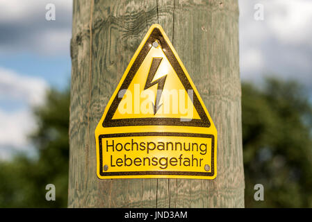 Deutsche Hochspannungs Schild montiert auf Holzstab mit grüner Baum im Hintergrund Stockfoto