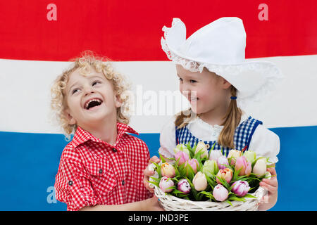 Niederländische Mädchen und jungen tragen traditionelle Tracht, Kleid und Hut Holding Korb mit Tulpen auf der Flagge der Niederlande. Kinder mit souve Stockfoto