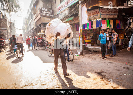 Ein Mann trägt eine schwere und unangenehme Last auf seinen Schultern durch die Straßen von Chandni Chowk, Märkte eines der belebtesten und ältesten in Delhi, Indien. Stockfoto