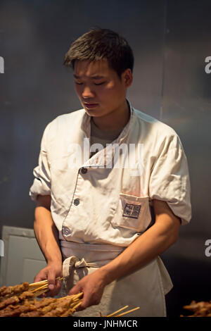 Chinesischen Verkäufer Zubereitung von Fleisch am Spieß auf traditionellen Lebensmittelmarkt. Wangfujing, Chaoyang District, Beijing, China, 5. April 2016 Stockfoto