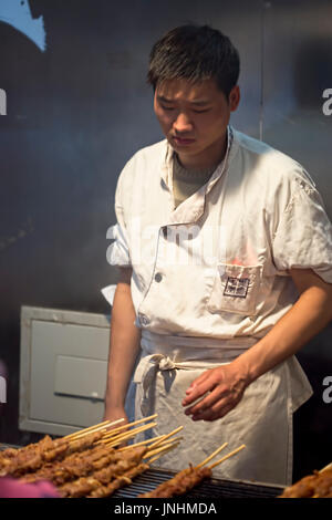 Chinesischen Verkäufer Zubereitung von Fleisch am Spieß auf traditionellen Lebensmittelmarkt. Wangfujing, Chaoyang District, Beijing, China, 5. April 2016 Stockfoto