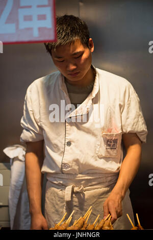 Chinesischen Verkäufer Zubereitung von Fleisch am Spieß auf traditionellen Lebensmittelmarkt. Wangfujing, Chaoyang District, Beijing, China, 5. April 2016 Stockfoto