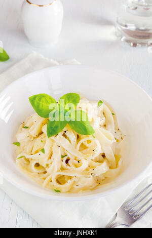 Alfredo-Tagliatelle-Nudeln mit Basilikum und schwarzem Pfeffer in weiße Schüssel - hausgemachte cremige Pasta mit Alfredo Soße Stockfoto