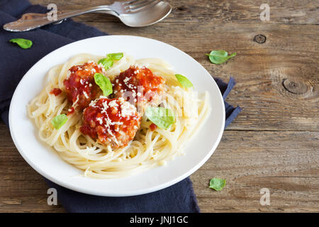Spaghetti Nudeln mit Fleischbällchen, Tomatensauce, geriebenem Parmesan und frischem Basilikum - gesunde hausgemachte italienische Pasta auf rustikalen hölzernen Hintergrund mit Stockfoto
