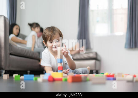 Asiatische junge Holz Spielzeug im Wohnzimmer mit Vater, Mutter und Tochter im Hintergrund zu spielen. Glückliche Familie. Stockfoto