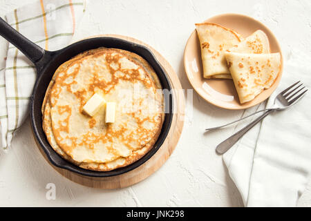 Hausgemachte Crepes mit Butter in Gusseisen Pfanne bei weißem Hintergrund - Kochen frische hausgemachte Frühstück Pfannkuchen Pfannkuchen essen Stockfoto