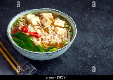 Japanische Ramen-Suppe mit Tofu auf dunklem Stein. Miso-Suppe mit Ramen-Nudeln und Tofu in Keramikschale, asiatische traditionelle Küche. Stockfoto