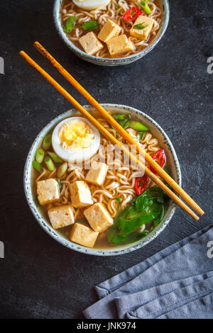 Japanische Ramen-Suppe mit Tofu und Ei auf dunklem Stein. Miso-Suppe mit Ramen-Nudeln und Tofu in Keramikschale, asiatische traditionelle Küche. Stockfoto