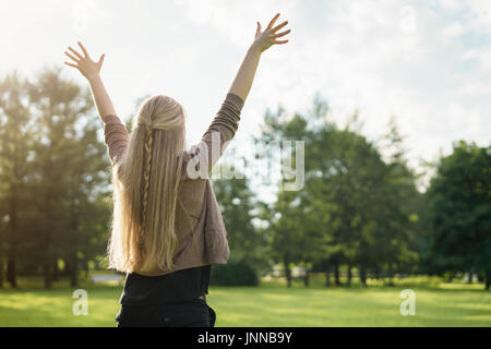 Weibliche Teenager-Mädchen von hinten stehend im Park mit Arme zum Himmel gestreckt Stockfoto