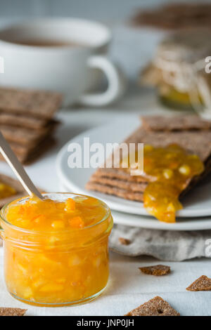 Nahaufnahme der Orangenmarmelade in Glas und braune Roggen Knäckebrot (schwedische Kekse) mit Verbreitung Marmelade darauf, auf weißem Hintergrund. Süße Snacks und Frühstück Stockfoto