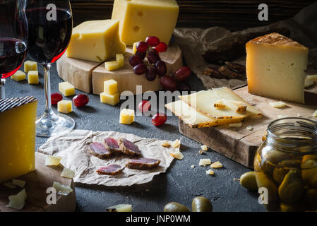 Käseplatte von gehackten Hartkäse (schwedische, spanische Manchego) und in Scheiben geschnittenen italienischen Pecorino Toscano auf Holzbrettern mit grünen Oliven in Glas ja Stockfoto