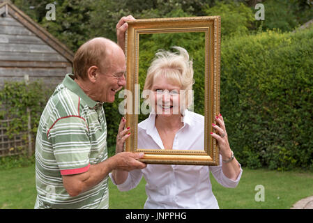 Älteres Ehepaar mit einem Bilderrahmen in einem Garten spielen Stockfoto