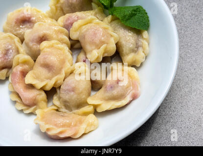 Knödel mit Kirschen, dekoriert mit Minze auf einem weißen Teller Stockfoto