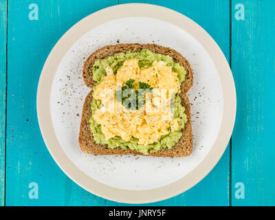 Unkenntlich gemacht, Eiern und Avocado auf geröstetem Vollkornbrot Brown auf blauem Grund aus Holz Stockfoto