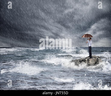 Geschäftsmann mit Regenschirm bei Sturm im Meer. Konzept des Versicherungsschutzes Stockfoto