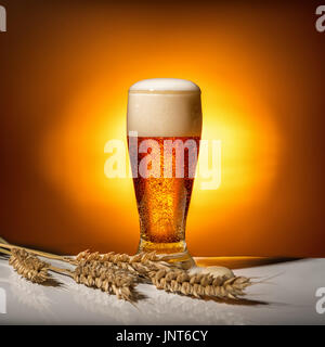 dunklem Glas Bier mit Ähren auf hellem Hintergrund, Oktoberfest-Konzept Stockfoto