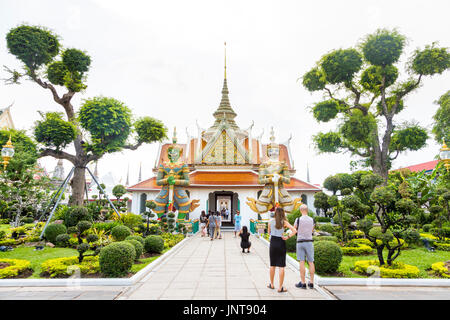 Der Eingang (Phra Ubosot) zu monastischen Viertel Komplexe mit riesigen Dämon zahlen und formgehölze Bäume am Wat Arun (Tempel der Morgenröte) in Bangkok, Thailand Stockfoto