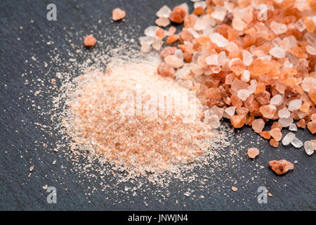 feine und grobe Kristalle von rosa Himalayasalz auf grauem Schiefer Stockfoto