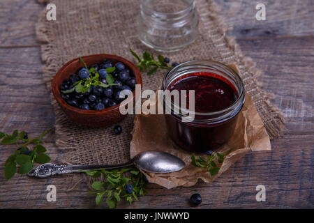 Blaubeeren Marmelade im Glas mit Beeren und Blätter über rustikalen Holztisch Stockfoto