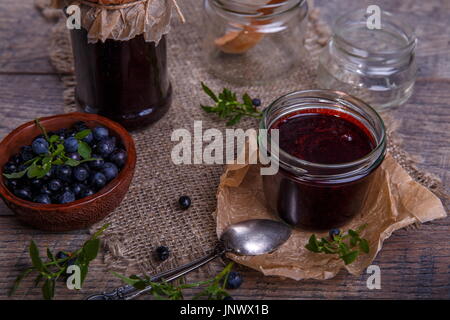 Blaubeeren Marmelade im Glas mit Beeren und Blätter über rustikalen Holztisch Stockfoto