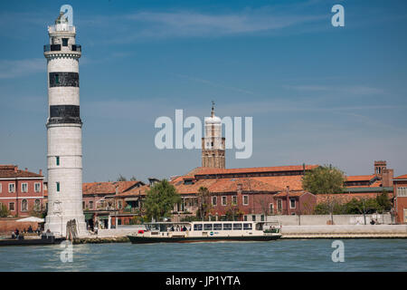 Murano, Venedig, Italien - 28. April 2012: Der Leuchtturm (Faro) auf Murano in der Lagune mit der Kirche von Pietro Martire hinter. Eine Vaporetto bringt und nimmt Passagiere. Stockfoto