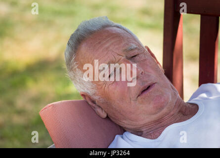 Ältere Mann auf Bank im Garten liegen und ruhen. Vorbereitung für siesta Stockfoto