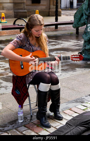 Eine junge südlichen irische Studentin Straßenmusikant Gitarre spielen und singen, etwas Geld verdienen an einem verregneten Tag in Dundee, Großbritannien Stockfoto