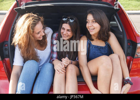 Freunde, eine gute Zeit und erfreuen sich an der Rückseite des Autos. Sie sind glücklich, weil Sie im Urlaub sind. Die Mädchen sind zu lächeln und zu lachen. Stockfoto