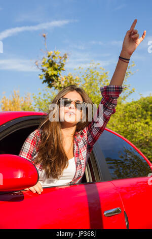 Porträt der glückliche junge Frau, die auf einem Road Trip lehnte sich aus dem Fenster des roten Auto. Stockfoto