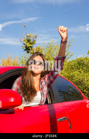 Porträt der glückliche junge Frau, die auf einem Road Trip lehnte sich aus dem Fenster des roten Auto. Stockfoto