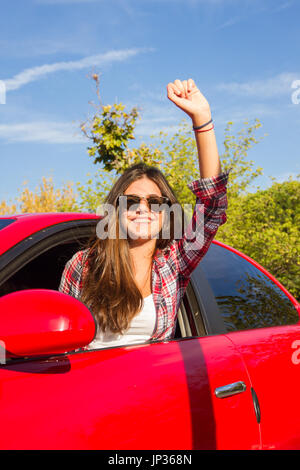 Porträt der glückliche junge Frau, die auf einem Road Trip lehnte sich aus dem Fenster des roten Auto. Stockfoto