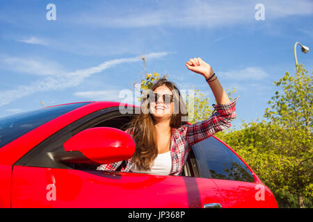 Porträt der glückliche junge Frau, die auf einem Road Trip lehnte sich aus dem Fenster des roten Auto. Stockfoto