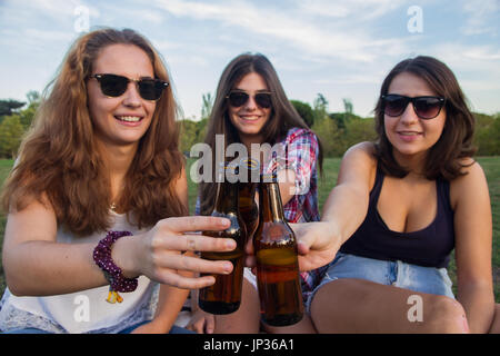 Die Mädchen genießen. Sie sind Freunde feiern den Urlaub eine gute Zeit Bier trinken in einem Park. Sie sind Toasten mit Flaschen. Stockfoto