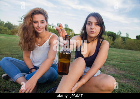 Zwei Mädchen, Freunde, Zigaretten rauchen und trinken Bier Flaschen in den Park an einem bewölkten Tag. Sie sind von der Feier und sind glücklich. Stockfoto