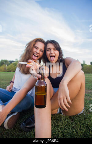 Zwei Mädchen, Freunde, Zigaretten rauchen und trinken Bier Flaschen in den Park an einem bewölkten Tag. Sie sind von der Feier und sind glücklich. Stockfoto